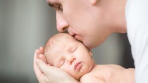 Padre sosteniendo y besando a su bebé recién nacido, baja de paternidad y permiso por nacimiento