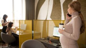 Mujer embarazada trabajando en la oficina mientras habla por teléfono, maternidad y carrera profesional