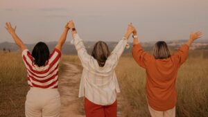 Tres mujeres de mediana edad cogidas de la mano y celebrando al aire libre, salud a partir de los 40 y 50 años