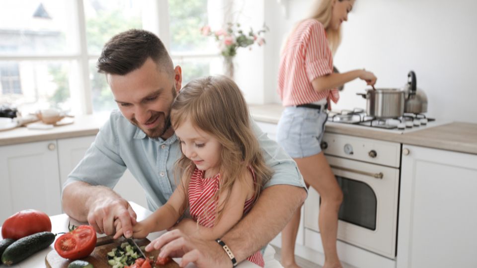 padre e hija cocinando juntos mientras la madre cocina al fondo